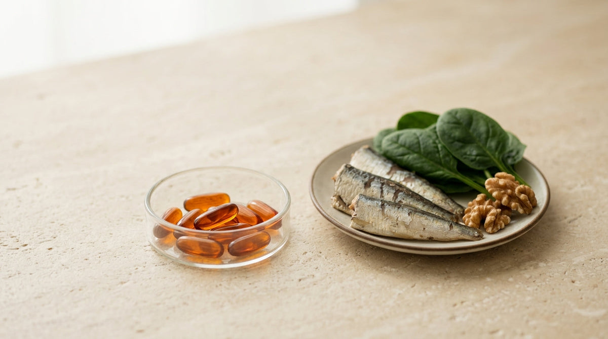A glass of water beside an amber supplement bottle and a small pile of soft-gel capsules on a pale stone counter